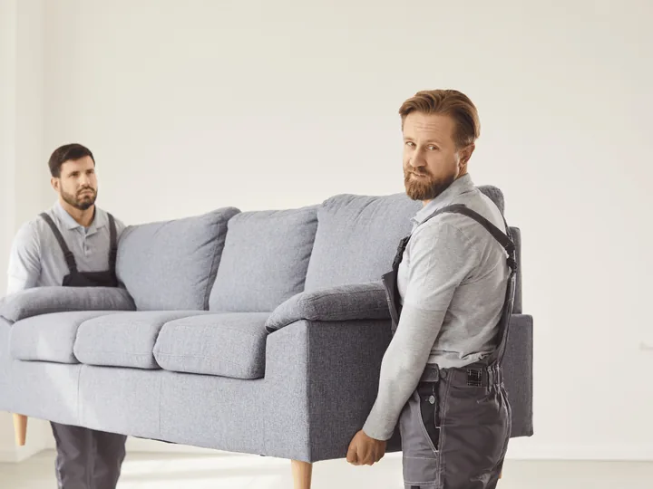 Seniorenwoning leegruimen: twee verhuizers dragen een bank die niet meegaat naar de nieuwe woning Seniorenwoning leegruimen: twee verhuizers dragen een bank die niet meegaat naar de nieuwe woning